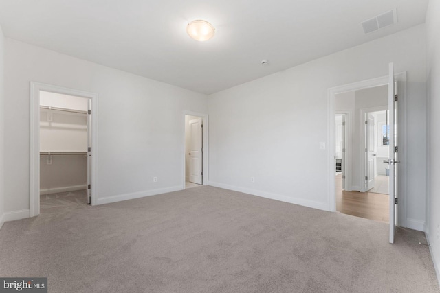 unfurnished bedroom with a closet, a spacious closet, baseboards, visible vents, and carpet