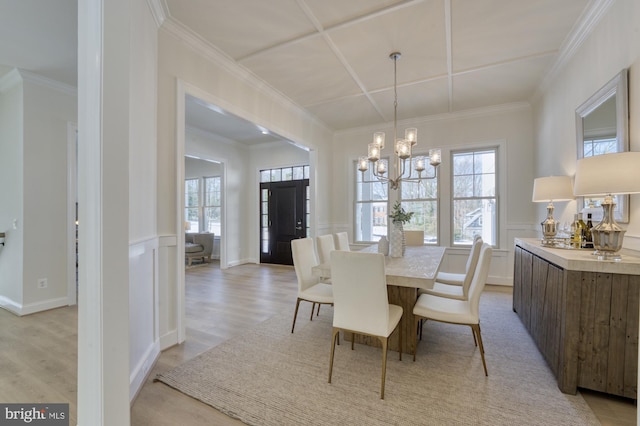 dining space featuring an inviting chandelier, a wainscoted wall, ornamental molding, and light wood-style floors