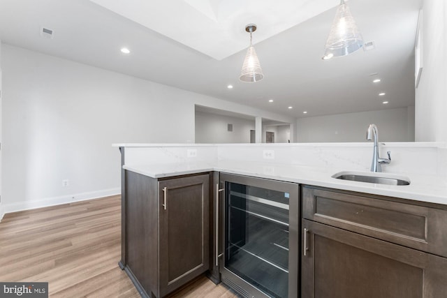 kitchen with dark brown cabinetry, a sink, wine cooler, and light wood finished floors