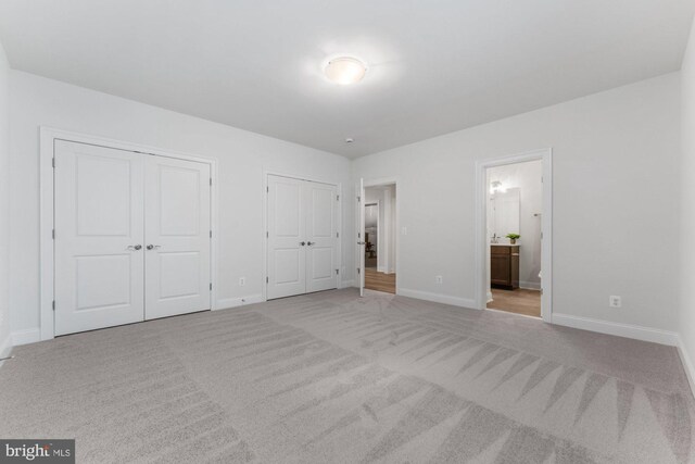 unfurnished bedroom with light colored carpet, ensuite bathroom, baseboards, and multiple closets