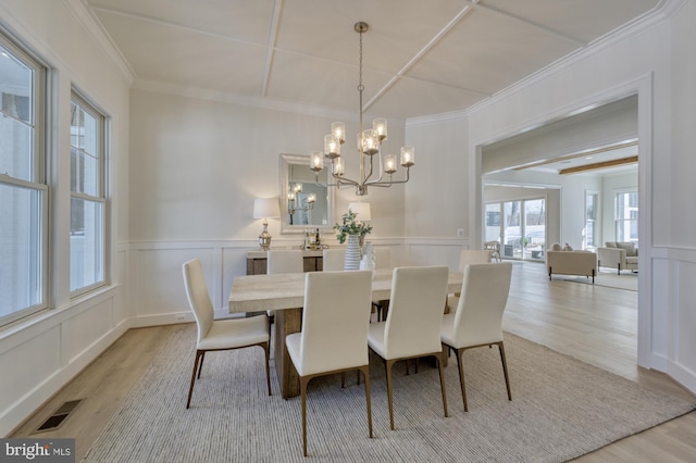 dining room featuring a decorative wall, visible vents, a chandelier, ornamental molding, and light wood-type flooring