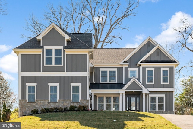 view of front of property with stone siding, roof with shingles, board and batten siding, and a front yard