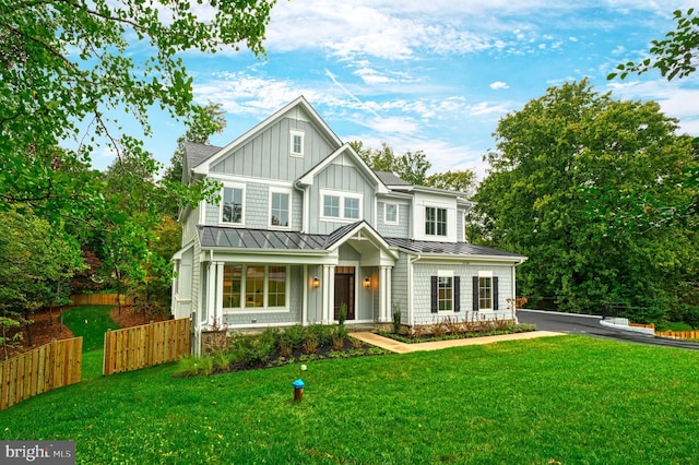 view of front of home with board and batten siding, a front yard, a standing seam roof, fence, and metal roof