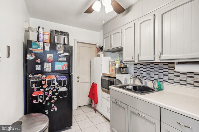 kitchen featuring light tile patterned flooring, sink, black fridge, ceiling fan, and decorative backsplash