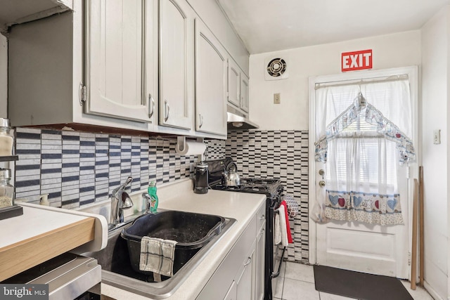 kitchen with light tile patterned flooring, sink, tasteful backsplash, stove, and white cabinets