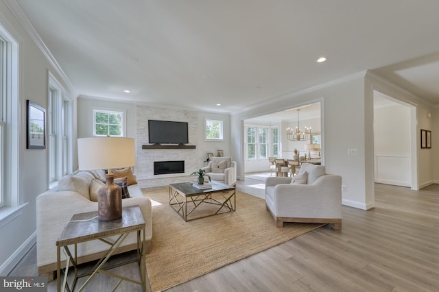 living area with light wood finished floors, recessed lighting, ornamental molding, a stone fireplace, and a chandelier