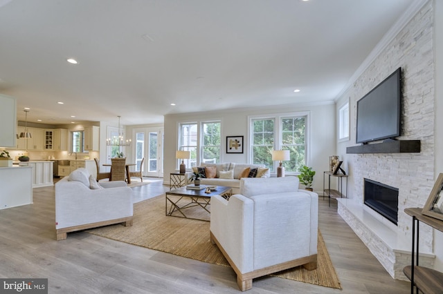 living area with recessed lighting, light wood-style floors, ornamental molding, a stone fireplace, and a chandelier