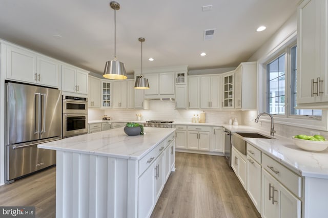 kitchen with a center island, stainless steel appliances, hanging light fixtures, glass insert cabinets, and white cabinets