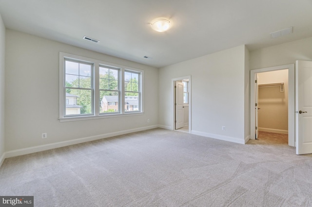 unfurnished bedroom featuring visible vents, a spacious closet, light carpet, ensuite bath, and baseboards