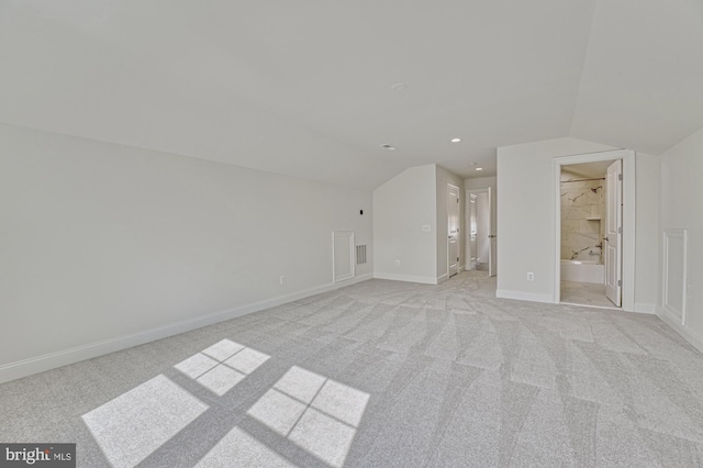 unfurnished bedroom with lofted ceiling, connected bathroom, light colored carpet, and baseboards