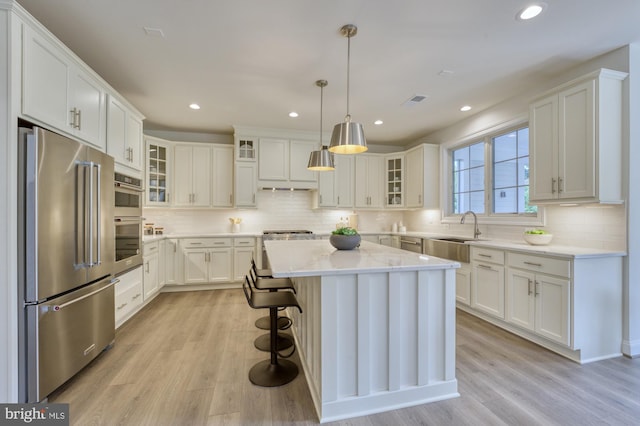 kitchen with glass insert cabinets, appliances with stainless steel finishes, pendant lighting, and a center island