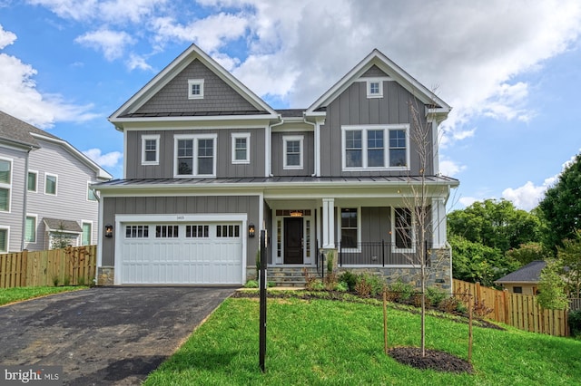 craftsman house featuring aphalt driveway, board and batten siding, a standing seam roof, fence, and a front lawn