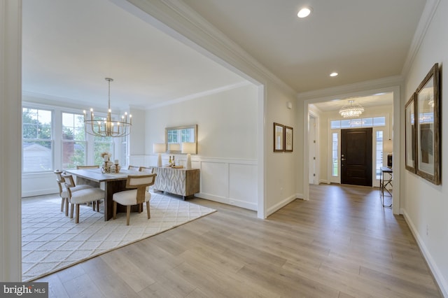 dining room with a decorative wall, light wood-style flooring, ornamental molding, wainscoting, and a chandelier