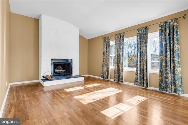 unfurnished living room featuring wood-type flooring, vaulted ceiling, and a brick fireplace