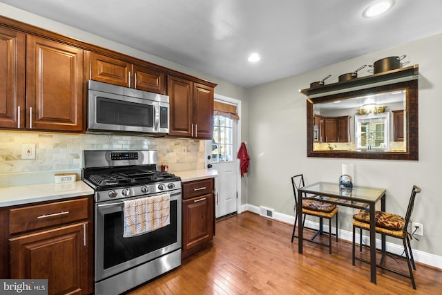 kitchen featuring baseboards, dark wood-type flooring, stainless steel appliances, light countertops, and backsplash