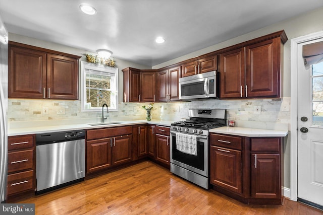 kitchen featuring stainless steel appliances, tasteful backsplash, light countertops, a sink, and wood finished floors