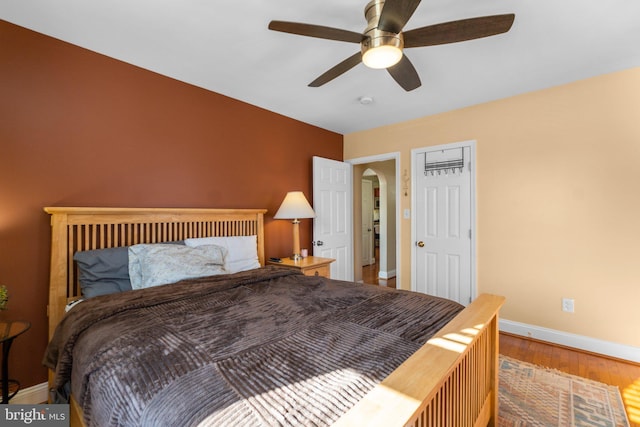 bedroom featuring a ceiling fan, baseboards, arched walkways, and wood finished floors