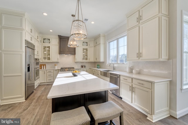 kitchen featuring light wood finished floors, appliances with stainless steel finishes, glass insert cabinets, a center island, and pendant lighting