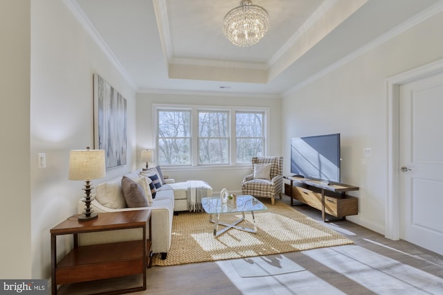 living area featuring baseboards, wood finished floors, a tray ceiling, crown molding, and a chandelier