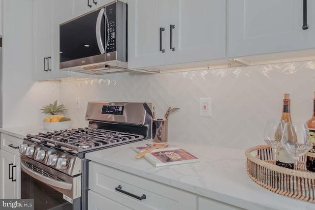 kitchen featuring stainless steel appliances, white cabinets, backsplash, and light stone counters