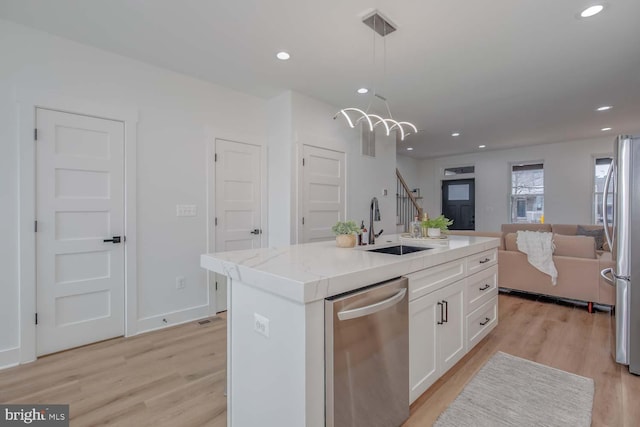 kitchen featuring stainless steel appliances, a sink, white cabinetry, open floor plan, and light wood finished floors