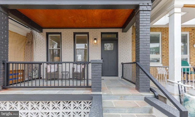 view of exterior entry with covered porch and brick siding