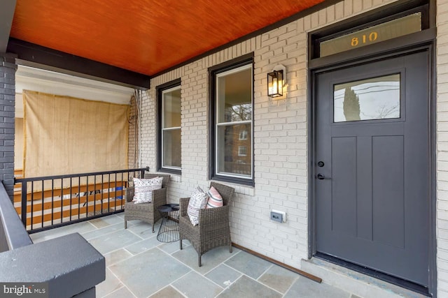 doorway to property featuring a porch and brick siding