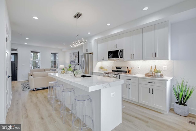 kitchen featuring light stone counters, stainless steel appliances, light wood-style floors, open floor plan, and a center island with sink