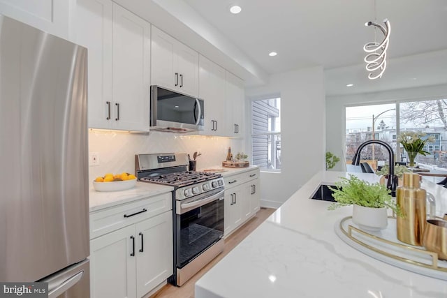 kitchen featuring stainless steel appliances, tasteful backsplash, light stone countertops, and white cabinets