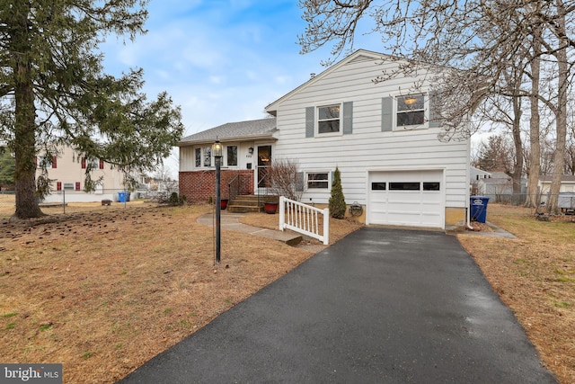 tri-level home featuring a garage, aphalt driveway, and fence