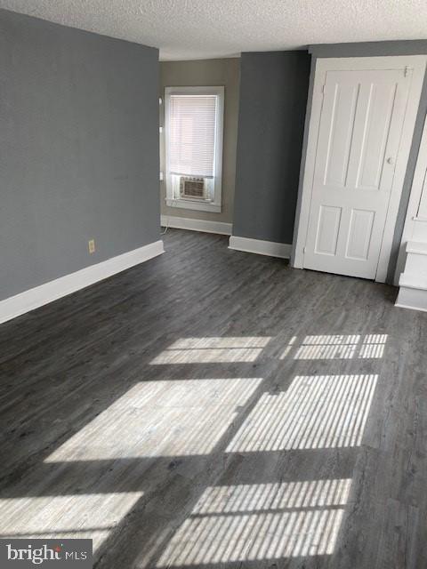 unfurnished bedroom featuring dark hardwood / wood-style flooring, cooling unit, and a textured ceiling