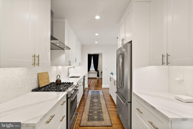 kitchen with high end appliances, a sink, dark wood-type flooring, white cabinetry, and wall chimney exhaust hood