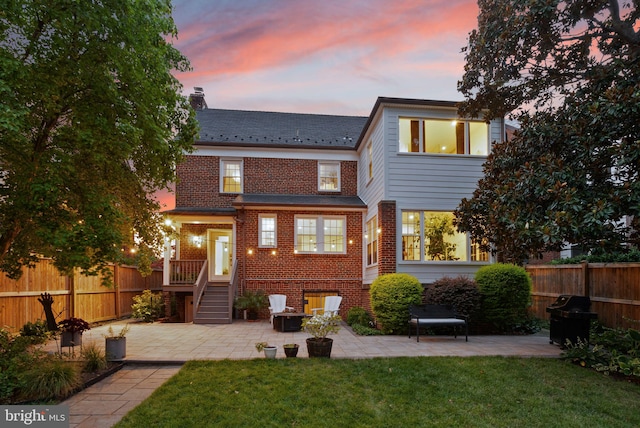 back of house featuring brick siding, a chimney, a patio area, and a high end roof