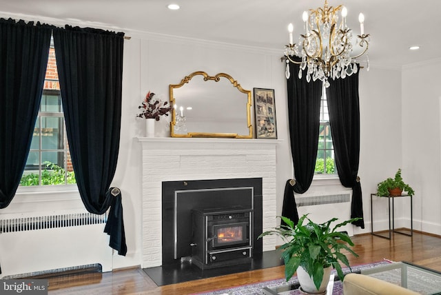 living area featuring radiator, ornamental molding, a chandelier, a brick fireplace, and wood finished floors