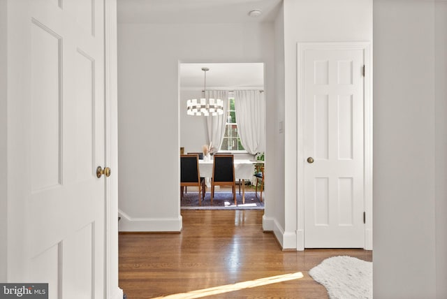hallway featuring wood finished floors, baseboards, and a chandelier