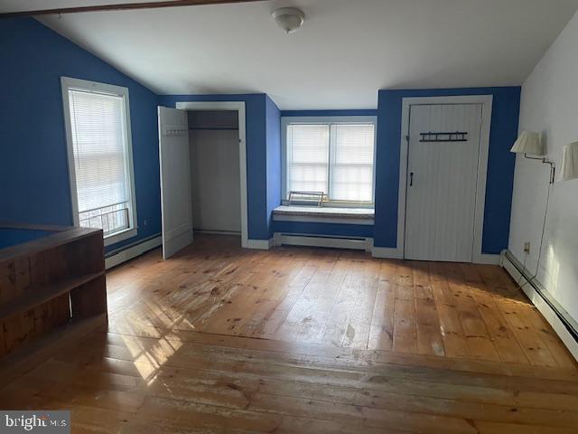 unfurnished bedroom with hardwood / wood-style floors, lofted ceiling, and a baseboard heating unit