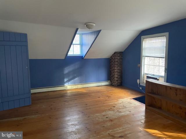 bonus room with a baseboard heating unit, lofted ceiling, cooling unit, and light hardwood / wood-style flooring