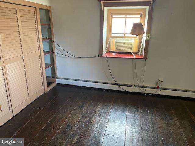 unfurnished bedroom featuring cooling unit, dark hardwood / wood-style floors, and baseboard heating