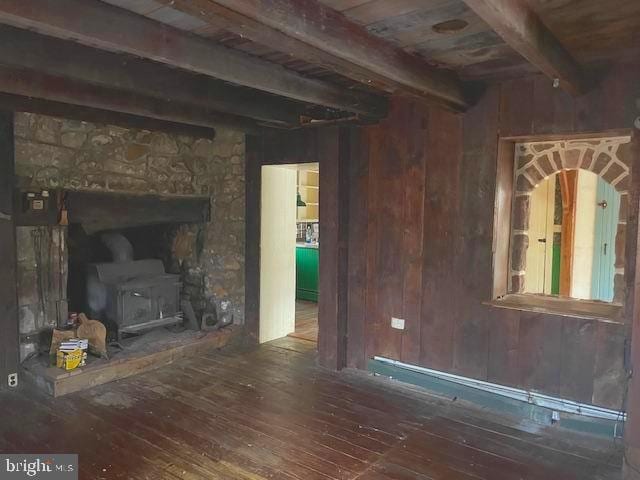 unfurnished living room with beam ceiling, wooden walls, dark wood-type flooring, wood ceiling, and a wood stove