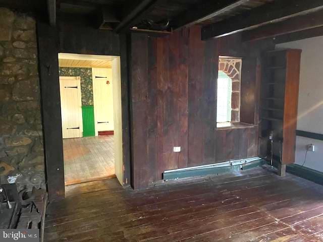 empty room with beam ceiling, dark wood-type flooring, and wooden walls