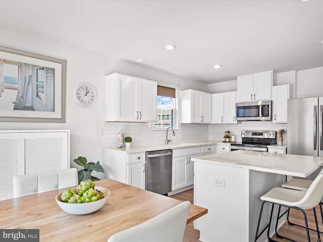 kitchen with a breakfast bar, a sink, white cabinets, appliances with stainless steel finishes, and a center island