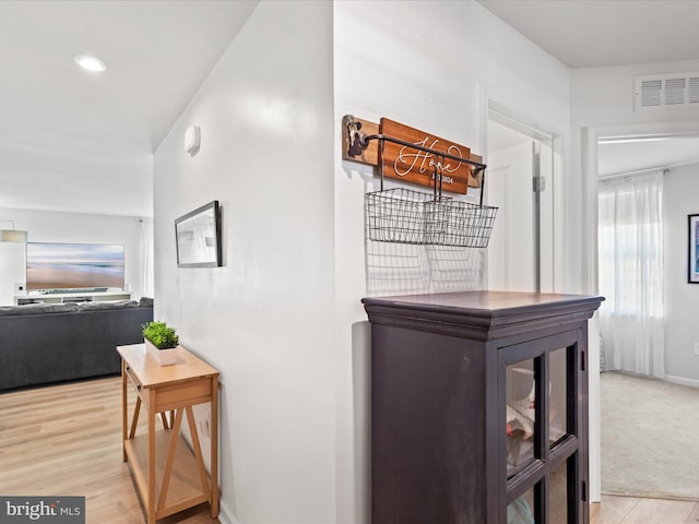 hallway with light carpet, visible vents, light wood-type flooring, and baseboards