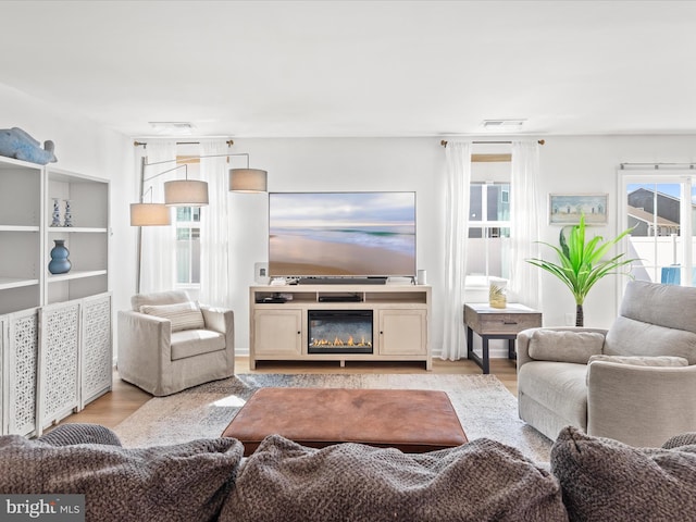 living room with a glass covered fireplace, visible vents, and wood finished floors