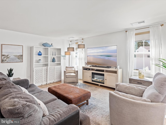 living area with a glass covered fireplace, visible vents, and light wood-style flooring