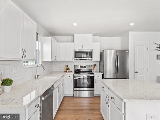 kitchen featuring white cabinets, appliances with stainless steel finishes, light wood-style floors, and a sink