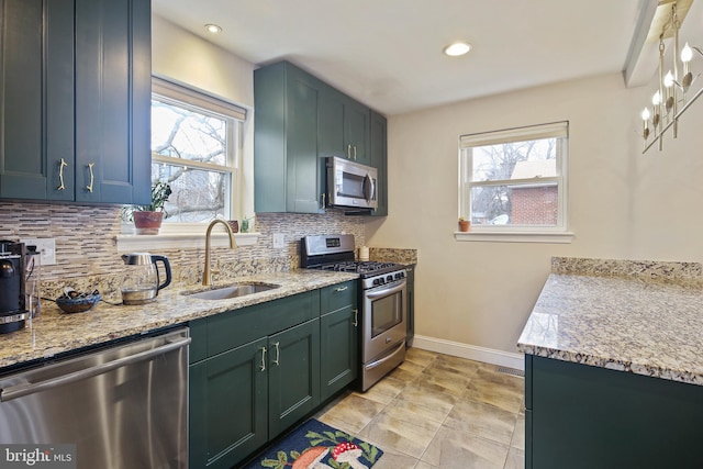 kitchen featuring baseboards, appliances with stainless steel finishes, light stone counters, a sink, and backsplash