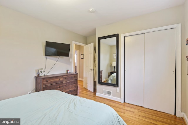 bedroom with light wood-style floors, baseboards, visible vents, and a closet