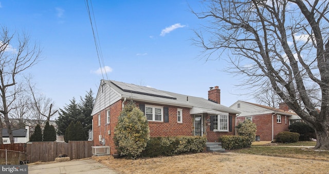 view of front of house with brick siding, fence, a chimney, and central air condition unit