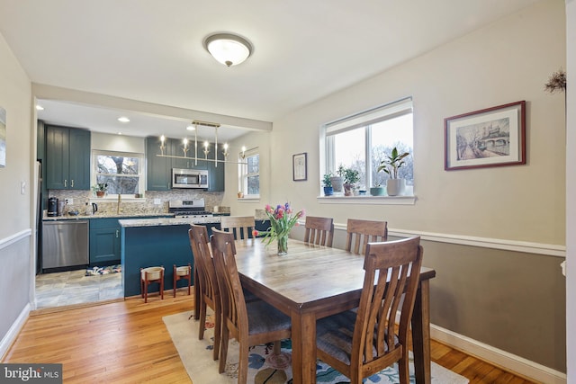 dining space with light wood finished floors, baseboards, and an inviting chandelier