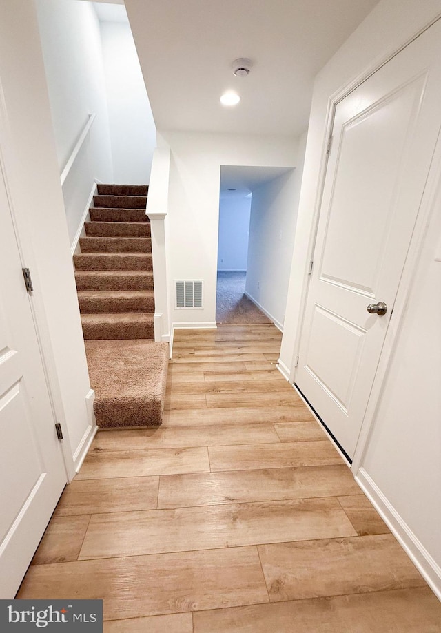 hallway featuring recessed lighting, visible vents, baseboards, stairs, and light wood-style floors